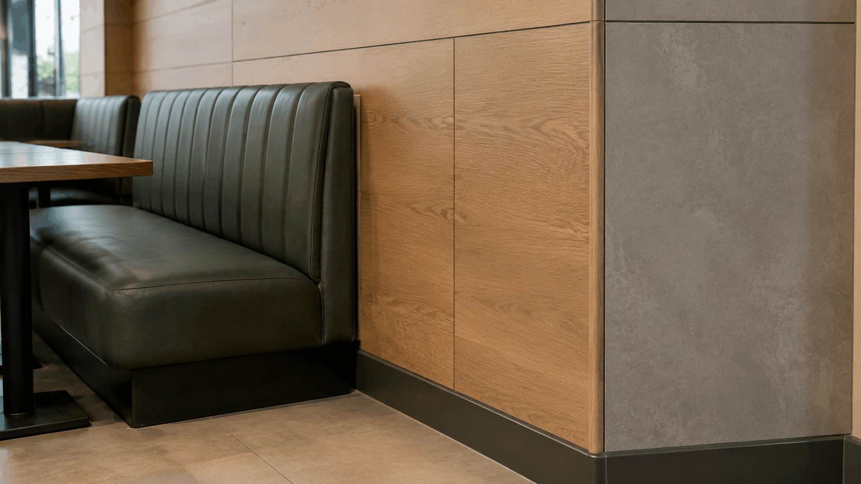 Close-up of dado-height timber wall panelling above a dark leather booth, with a concrete-look panel section beside it